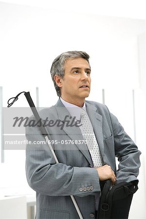 Visually impaired businessman holding white can, digging in briefcase