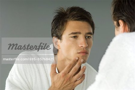 Man in bathrobe looking in mirror, inspecting skin