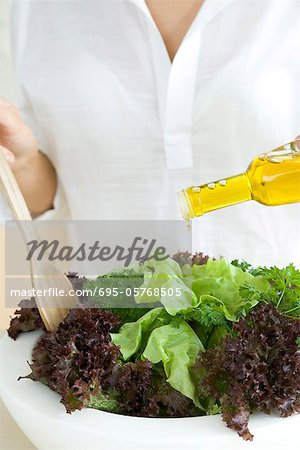 Woman preparing salad, pouring olive oil dressing