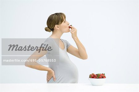 Pregnant woman eating strawberries, side view