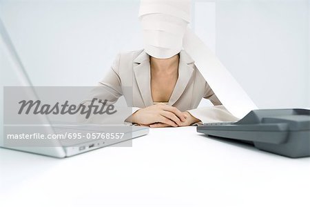 Professional woman sitting at desk, paper from adding machine wrapped around face