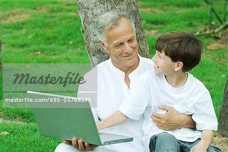 Boy sitting on grandfather's lap, using laptop computer