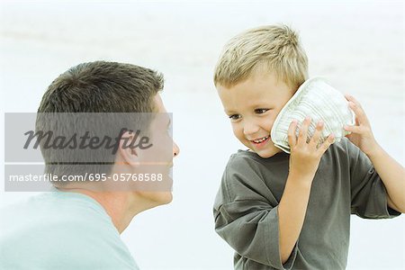 Père et fils à la plage, garçon écoute de coquillage