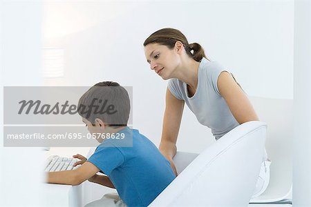 Boy typing on keyboard, mother looking over shoulder