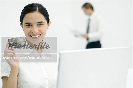 Jeune femme brandissant des cartes de crédit, souriant à la caméra