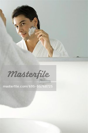 Man looking at himself in mirror, shaving, wearing bathrobe