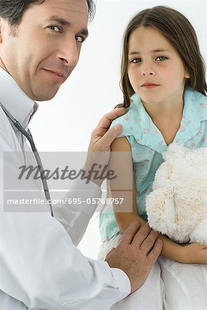 Pediatrician comforting little girl, smiling over shoulder at camera