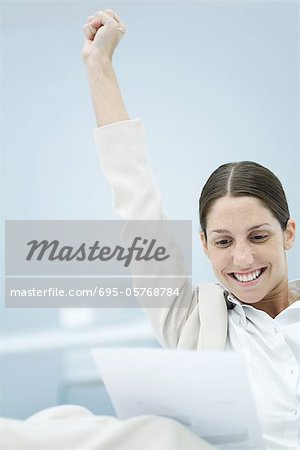 Young businesswoman reading document, raising one arm in the air