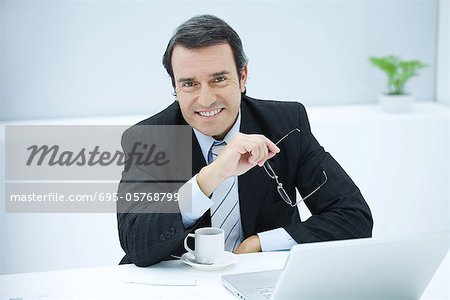 Businessman sitting at desk with coffee cup, smiling at camera