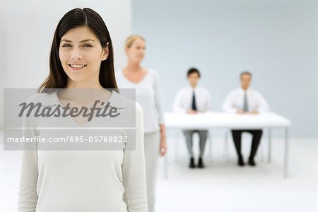 Professional woman smiling at camera, colleagues in background