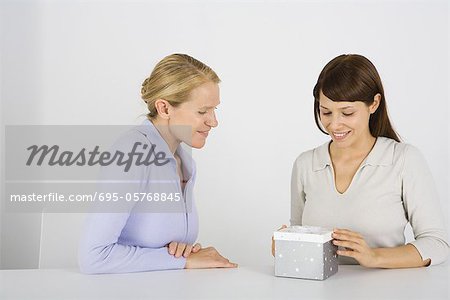 Two women sitting at table, one opening gift, both smiling