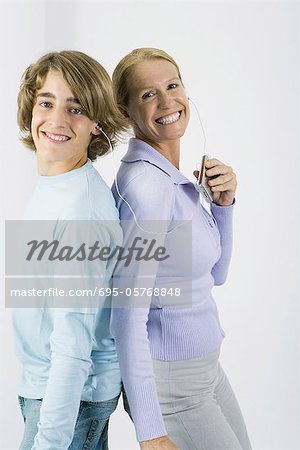 Mère et fils adolescent ensemble à l'écoute de MP3 player, debout dos à dos, souriant à la caméra