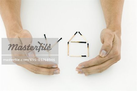 Hands protecting burnt matches arranged in shape of house and tree