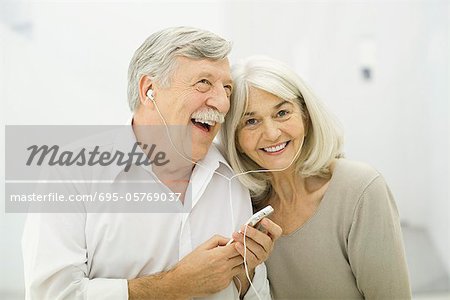 Senior couple listening to MP3 player together, woman smiling at camera