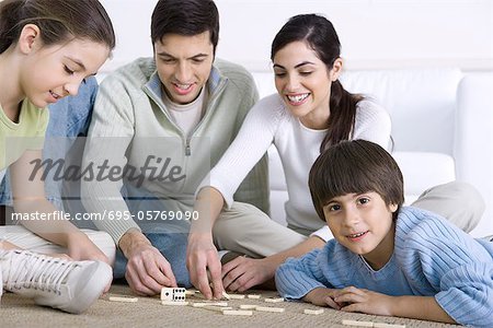 Family seated on floor playing dominoes together, boy smiling at camera