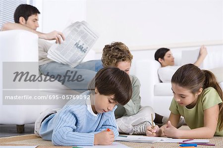 Enfants Coloriage sur le plancher dans la salle de séjour, parents de lecture en arrière-plan