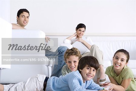 Familie zusammen im Wohnzimmer, Eltern, die Kinder auf dem Boden, liegend in die Kamera lächelnd auf Sofa, sitzen