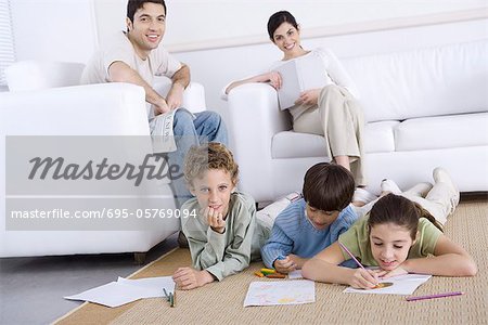 Three children coloring on the floor in living room, parents relaxing in background