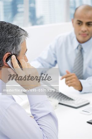 Les hommes d'affaires ayant une réunion au bureau, l'homme au premier plan, parlait au téléphone cellulaire