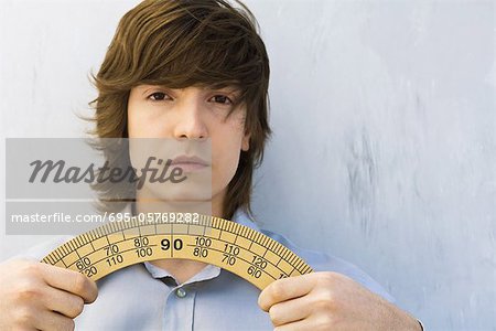 Young man holding protractor in both hands, looking at camera