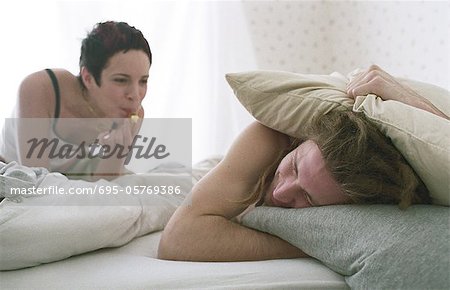 Young woman blowing whistle, awakening sleeping young man