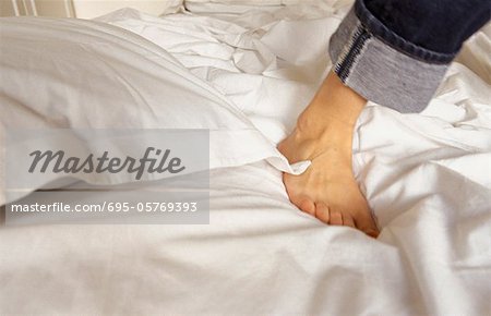 Foot of person standing on unmade bed, cropped view