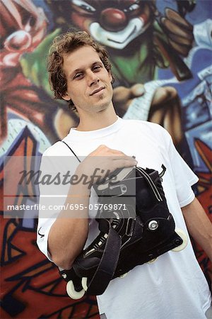 Male with pair of inline skates hanging over shoulder standing in front of wall mural