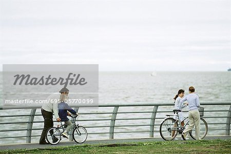 Family riding bicycles together at seaside park, father helping son learn to ride