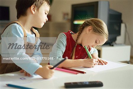Siblings drawing with colored pencils, little boy pausing to look over sister's shoulder