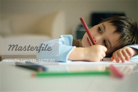 Little boy pausing while drawing, resting head on arm