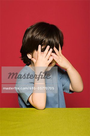 Little boy covering face with hands, peeking through fingers at camera