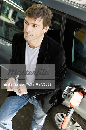 Homme à la station-service, appuyé contre la voiture en attente pour le réservoir d'essence remplir