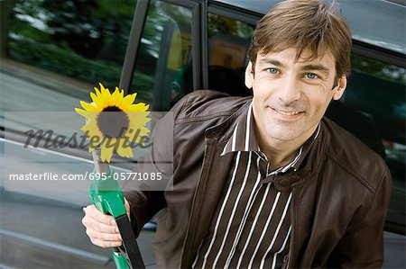 Man at gas station holding gas nozzle with sunflower emerging from end