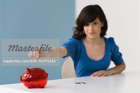 Teenage girl putting coin in piggy bank