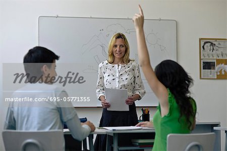 High school teacher in classroom, one student raising hand