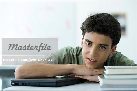 Élève du secondaire masculin assis au comptoir avec la tête appuyée sur les bras, portrait