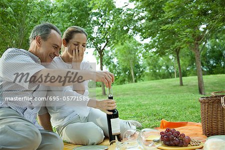 Mature couple having picnic outdoors, opening bottle of wine