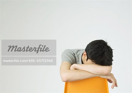 Young man sitting with head down on back of chair