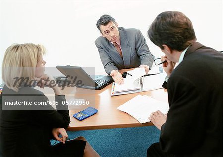 Two businessmen and a businesswoman sitting at desk, examining documents