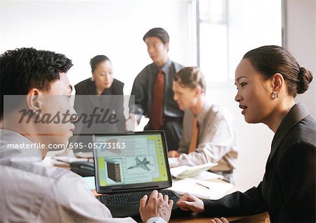 Business associates in front of computer screen, three people in background