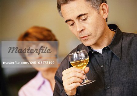 Man holding und Blick auf Glas Wein, Frau verschwommen im Hintergrund, Kopf und Schultern, close-up