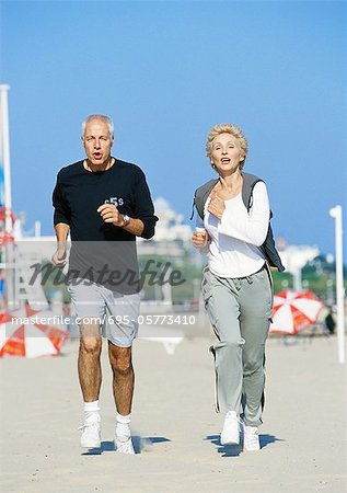 Mature couple jogging on beach, front view, full length