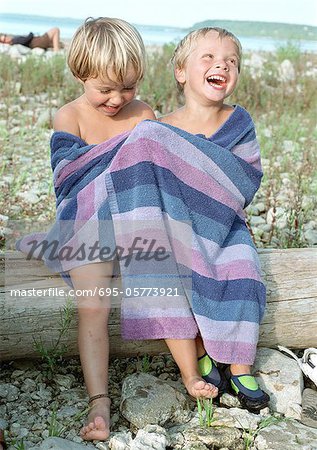 Fille et garçon dans la serviette de bain assis sur journal, souriant