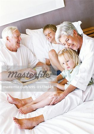 Grands-parents et enfants assis sur le lit, homme tenant le plateau de petit déjeuner