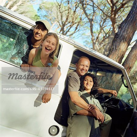 Portrait de famille, les enfants collent têtes par van fenêtre, parents à ouvrir la porte du van