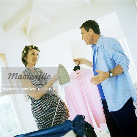 Mature couple facing each other, man holding shirt, woman handing him iron