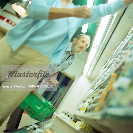 Man and woman in supermarket, man holding shopping basket