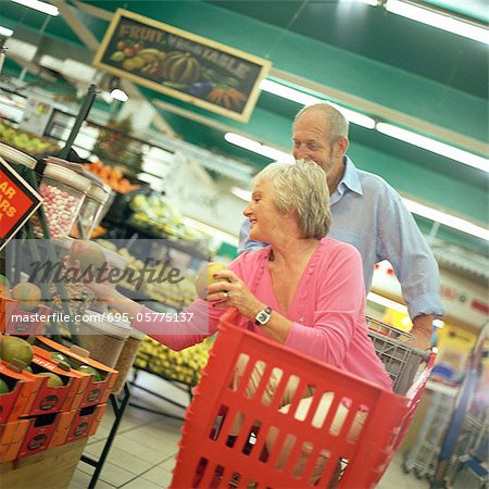 Mature couple in supermarket, woman in shopping cart choosing fruit
