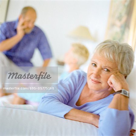 Mature woman looking into camera, fist against cheek, couple talking in background