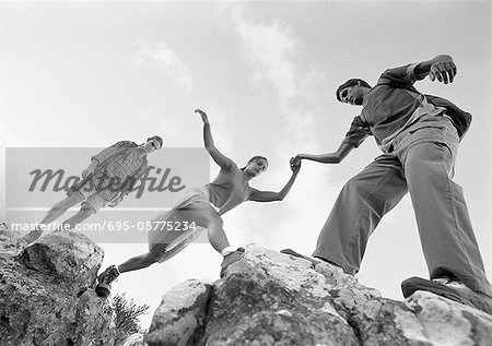 Drei Jugendliche Klettern auf den Felsen, Frau geholfen wird, low Angle View, b&w.